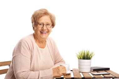 Bir kahve masada oturan ve üzerinde izole beyaz arka plan gülümseyen yaşlı kadın