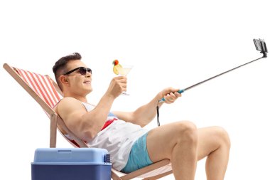 Turistik bir kokteyl bir güverte sandalyede oturuyor ve beyaz arka plan üzerinde izole bir sopa ile bir selfie alarak