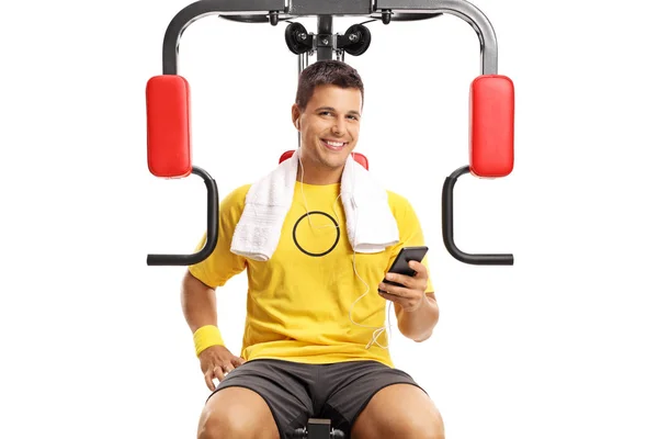 Jovem Sentado Uma Máquina Exercício Segurando Telefone Celular Isolado Fundo — Fotografia de Stock