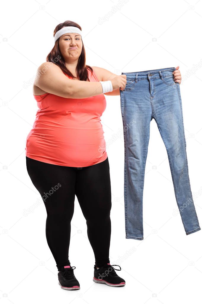 Full length portrait of an overweight woman in sportswear holding a pair of small jeans isolated on white background