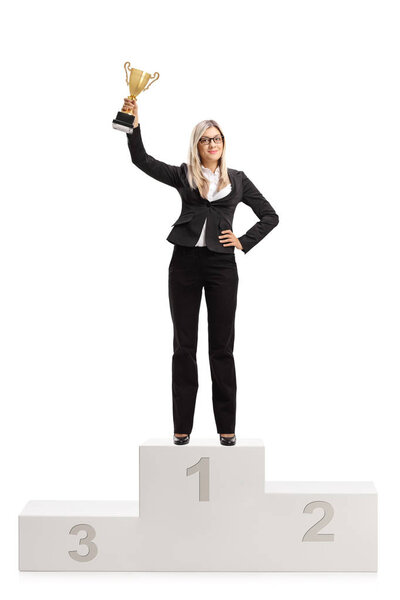 Full length portrait of a joyful businesswoman with a gold trophy standing on a winners pedestal isolated on white background