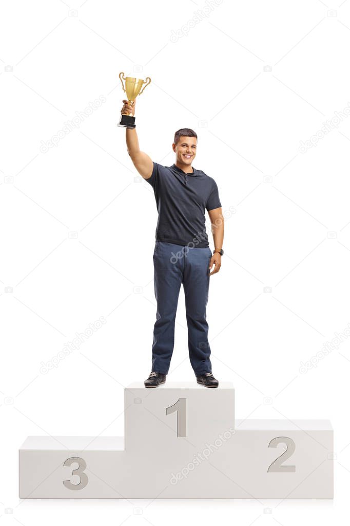 Full length portrait of a young man with a golden trophy standing on a winners pedestal isolated on white background