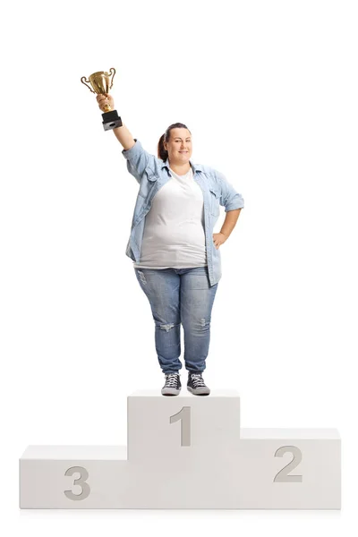 ゴールド トロフィー カップを保持していると 白い背景で隔離の勝者の台座の上に立っての肥満女性 — ストック写真