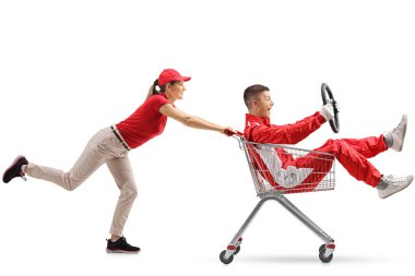 Female pushing a shopping cart with a teenage boy in a racing suit holding a steering wheel isolated on white background clipart