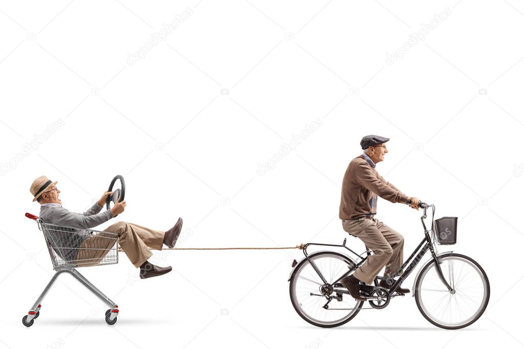 Elderly man riding a bicycle and pulling a shopping cart with a man holding a steering wheel suit isolated on white background