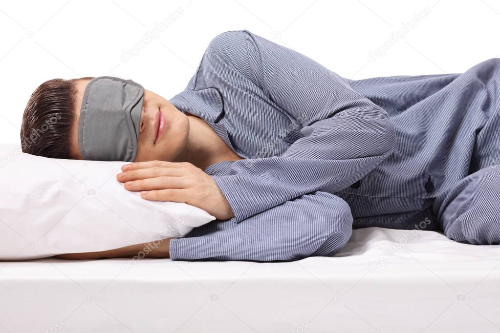 Young male sleeping on a pillow with eye mask isolated on white background