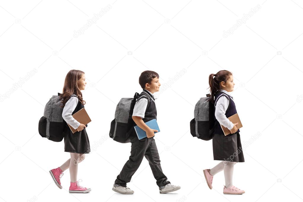 Full length profile shot of three schoolchildren with backpacks and books walking isolated on white background