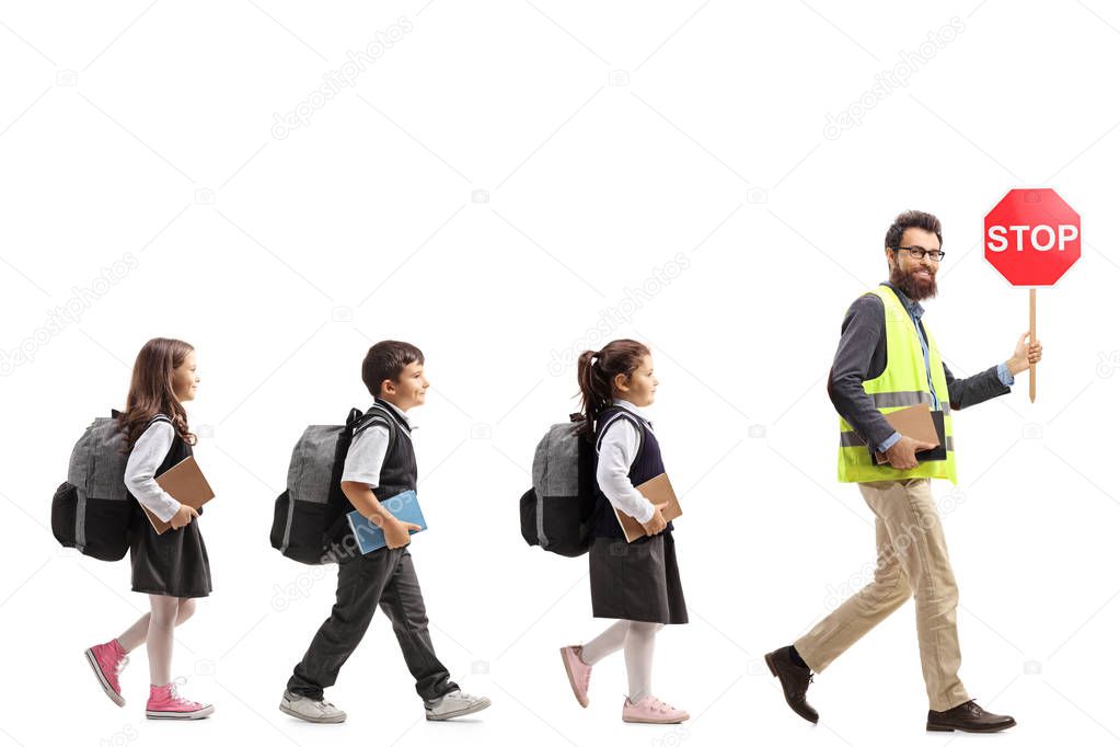 Full length profile shot of schoolchildren walking behind a teacher with a safety vest and a stop sign isolated on white background
