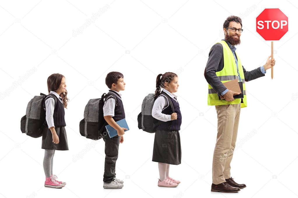 Full length profile shot of schoolchildren in line behind a teacher with a safety vest and a stop sign isolated on white background