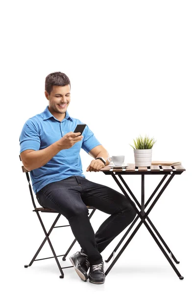 若い男のコーヒー テーブルに座っていると 白い背景で隔離の携帯電話を使用して — ストック写真