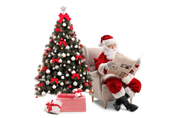 惊讶的圣诞老人坐在扶手椅上 看着一张在白色背景上被隔离的报纸 — 图库照片