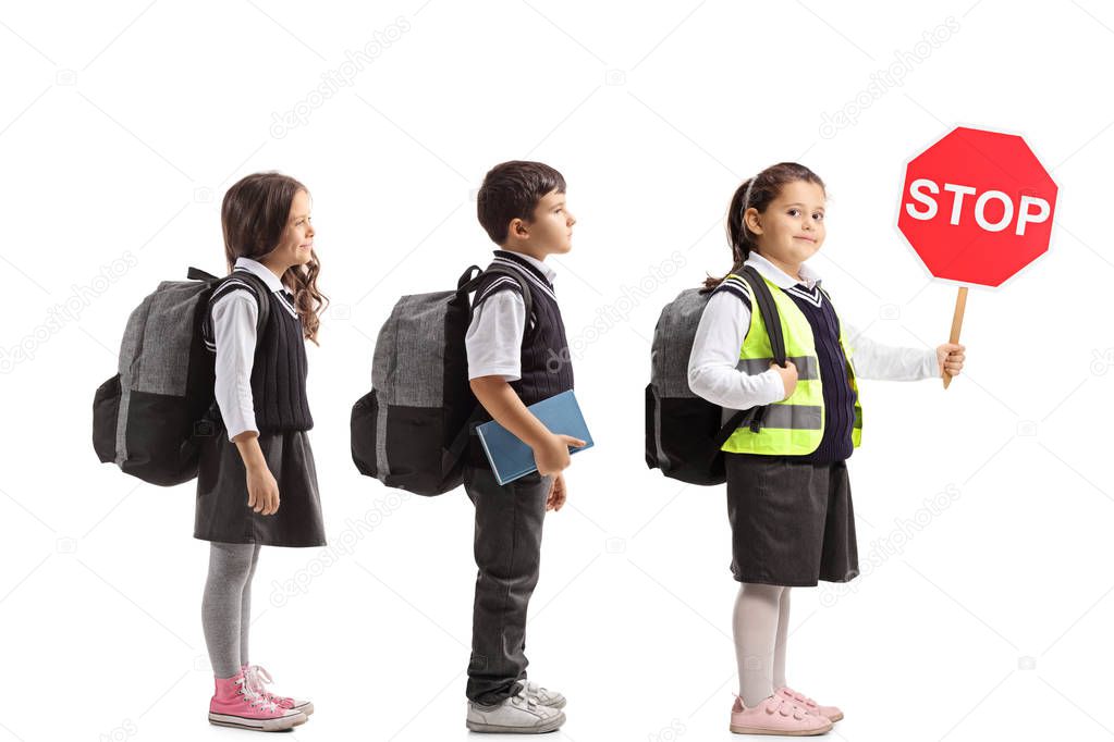 Full length shot of schoolchildren waiting in line with one of them wearing a safety vest and holding a stop sign isolated on white background