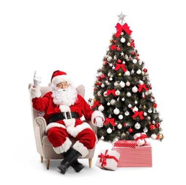 Noel Baba yukarı dönük bir koltuk ve bir şekilde dekore edilmiş bir Noel ağacı onun beyaz arka plan üzerinde izole yanında oturan