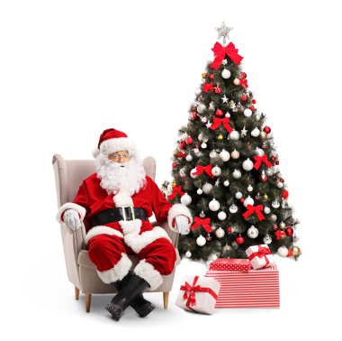 Sürpriz Noel Baba bir koltuk yanında beyaz arka plan üzerinde izole bir şekilde dekore edilmiş bir Noel ağacı ile oturuyor