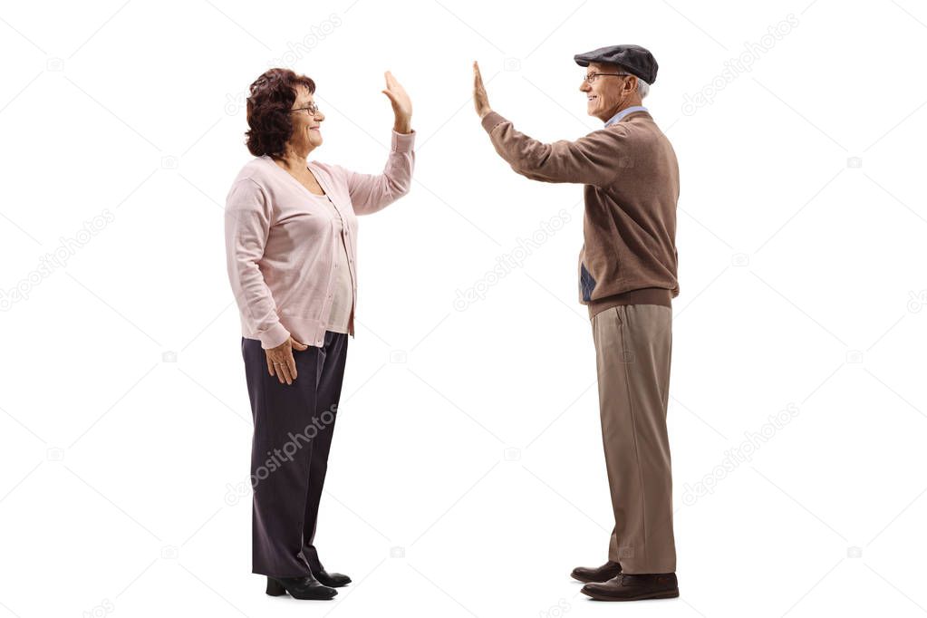 Full length profile shot of a senior woman high-fiving a senior man isolated on white background