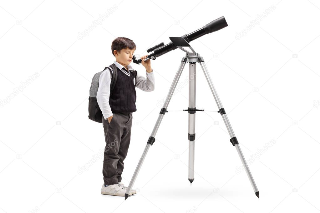 Full length shot of a schoolboy in a uniform looking through a telescope isolated on white background