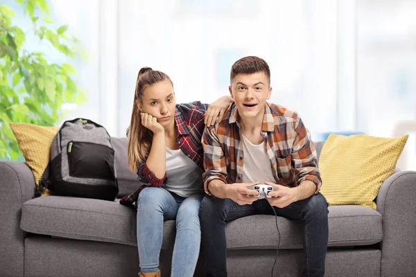 室内でソファーにビデオゲームで遊ぶ少年の隣に座って退屈十代の少女 — ストック写真