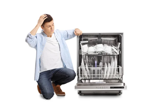 Angry Young Guy Kneeling Next Loaded Dishwasher Holding His Head — Stock Photo, Image