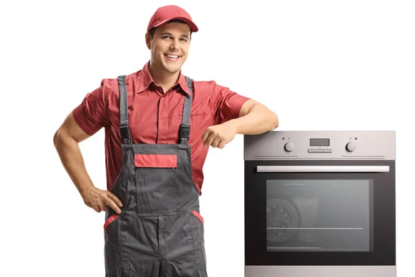 白い背景に分離された電気オーブンの横に制服立っての若い笑顔便利屋 — ストック写真
