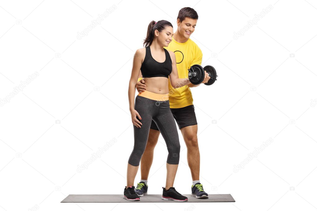 Full length portrait of a young female exercising with a dumbbell with the help of a male instructor isolated on white background