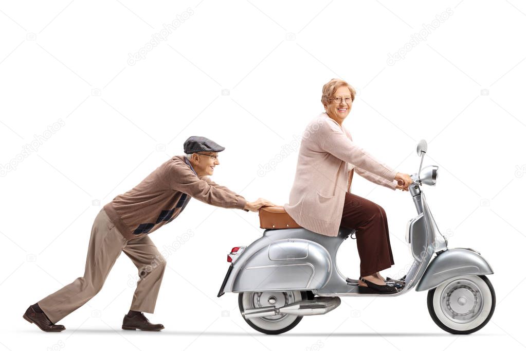 Full length profile shot of an elderly man pushing an elderly woman on a vintage motorbike isolated on white background