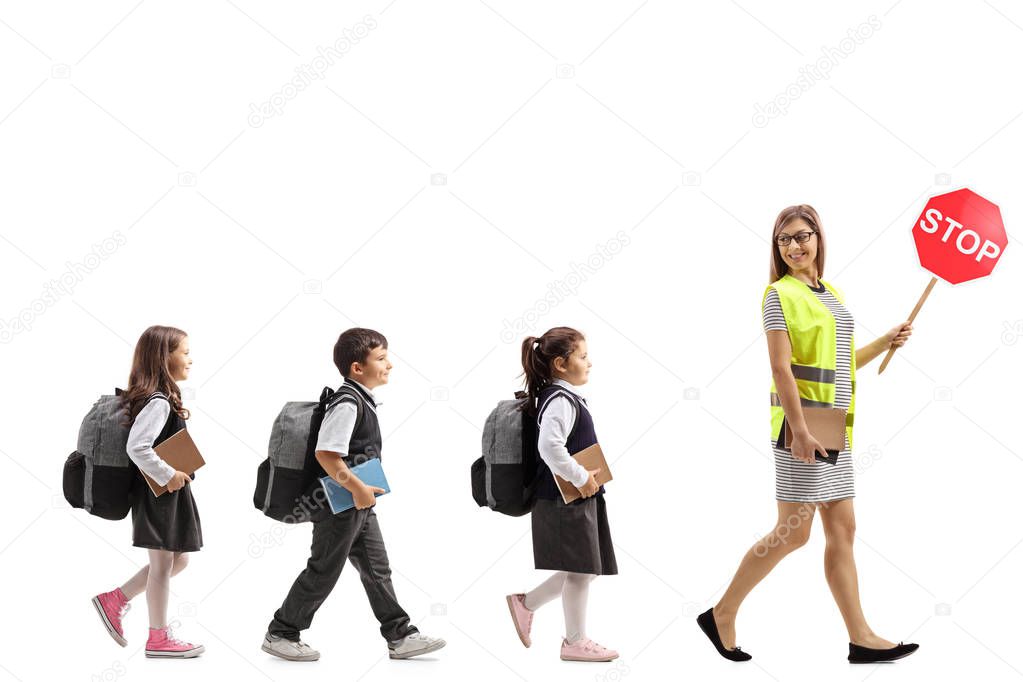 Full length profile shot of a school teacher with a safety vest and stop sign walking with schoolchildren  isolated on white background