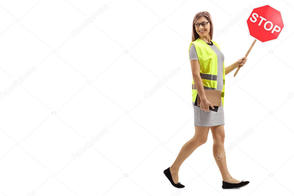Full length shot of a young woman with safety vest and stop sign walking and looking backwards isolated on white background