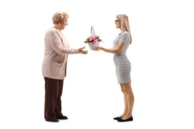 Yaşlı bir Bayan Beyaz arka plan üzerinde izole bir sepet çiçekli veren genç bir kadının tam uzunlukta profil vurdu