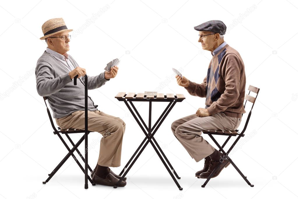 Full length shot of two senior men playing cards at a table isolated on white background