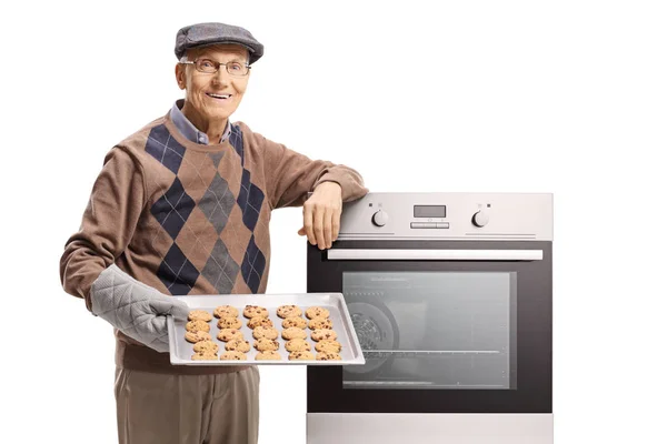 老人のクッキーとトレイを持って 白い背景に分離されたオーブンに傾いた — ストック写真