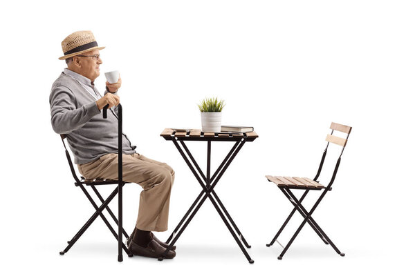 Full length profile shot of a senior man drinking coffee at a table isolated on white background