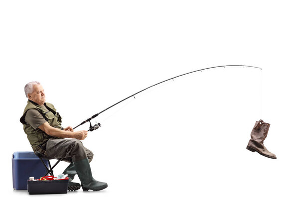 Full length shot of a fisherman on a chair with an old boot on the fishing rod isolated on white background