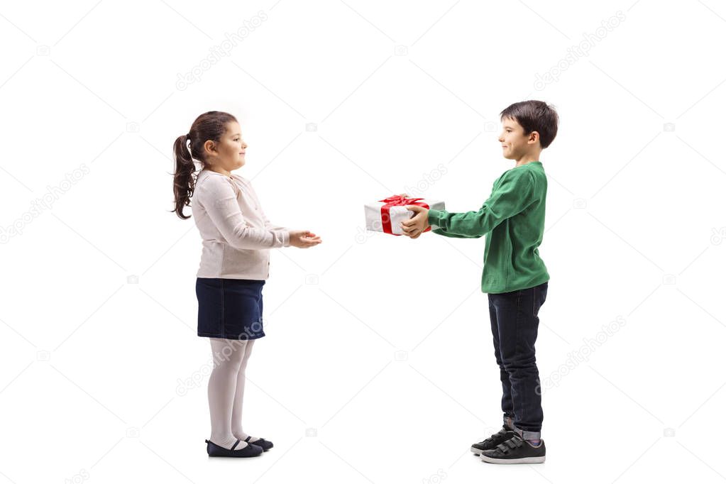 Full length profile shot of a little boy giving a present to a little girl isolated on white background