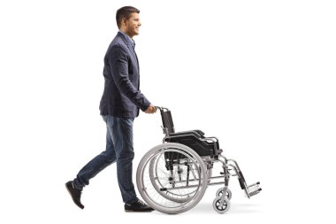 Tam uzunlukta profil atış genç bir adamın beyaz arka plan üzerinde izole boş bir tekerlekli sandalye itmek