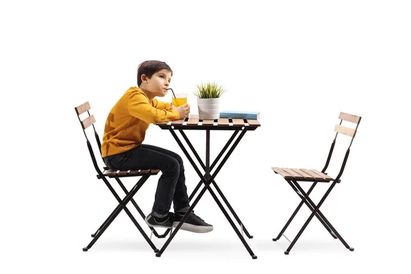一个小男孩喝果汁 独自坐在白色背景上的一张桌子旁的全长照片 — 图库照片
