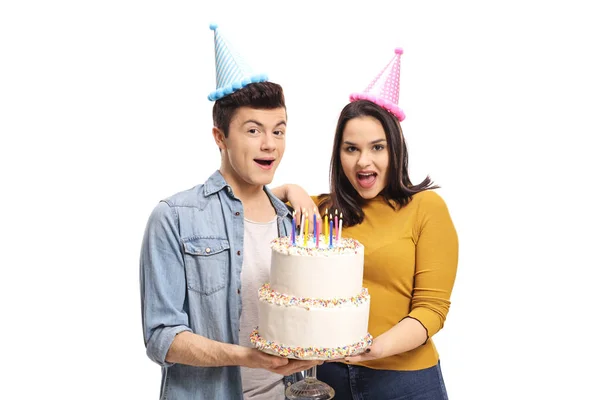 若い男性と女性の誕生日ケーキを押しながら円錐形のパーティの帽子を身に着けている白い背景の分離 — ストック写真