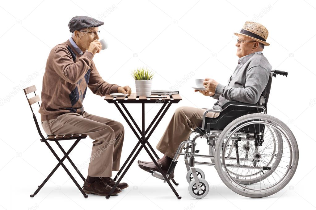 Full length profile shot of a senior man sitting and drinking coffee with a disabled man in a wheelchair isolated on white background