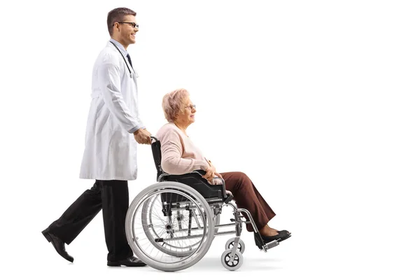 白い背景に分離された車椅子の年配の女性を押す若い男性医師の全身ショット — ストック写真