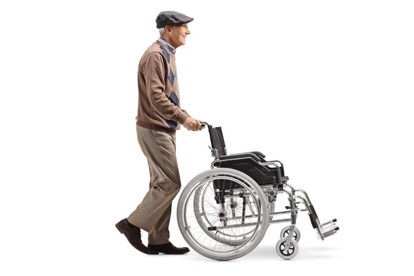 白い背景に分離された空の車椅子を押す老人の完全な長さのプロファイル ショット — ストック写真
