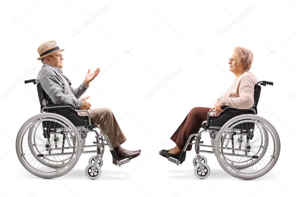 Full length profile shot of a senior gentlemen in a wheelchair talking to a senior woman in a wheelchair isolated on white background