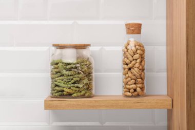 Ahşap raf, bir çay ile ve arka planda beyaz taşlarla Kabuklu fıstık ile diğer iki kavanoz