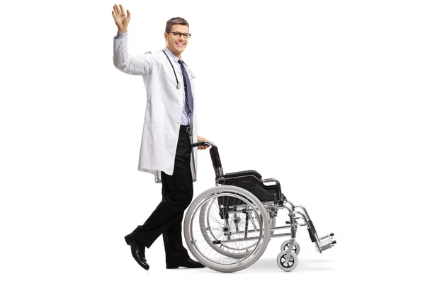 一个穿着实验室外套的年轻男医生的全长照片 挥舞着一个空轮椅 在白色背景上被隔离 — 图库照片