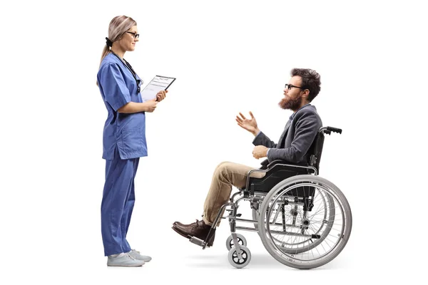 全長プロファイルショットを白い背景に分離された車椅子で髭の男に話す若い女性看護師の — ストック写真