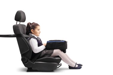 Full length profile shot of a little schoolgirl holding a backpack in a car seat with a seat belt isolated on white background clipart