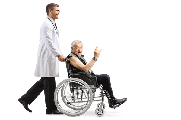 白い背景で隔離の車椅子サイン ロックン ロールをもうけて成熟した男性患者を押す若い男性医師の全身ショット — ストック写真