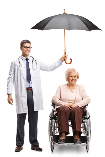 白い背景に分離された車椅子で年上の女の頭の上に傘を差し 男性医師の完全な長さの肖像画 — ストック写真