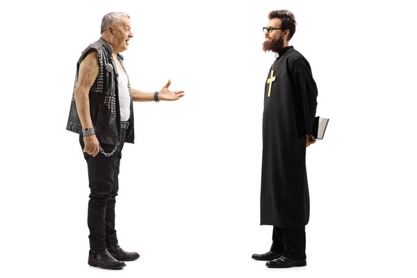 Full length profile shot of a mature male punker in a leather vest talking to a priest isolated on white background
