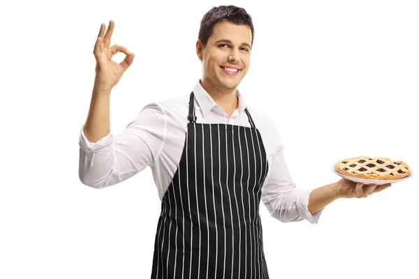 若い男を浮かべてパイを押しながら偉大な分離に白い背景を象徴する記号を作るエプロン — ストック写真