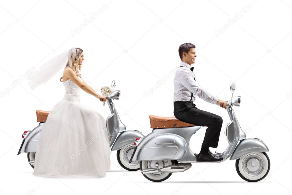Full length profile shot of a bride and groom riding vintage scooters isolated on white background
