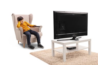 Tam uzunlukta atış bir koltuk beyaz arka plan üzerinde izole bir Tv önünde oturan sıkılmış bir küçük çocuk